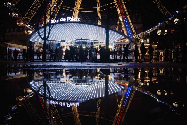 TOPSHOT - Visitors walk past the entrance to the ferris wheel at the seasonal Christmas market and fairground in the Jardin des Tuileries gardens in central Paris, on November 24, 2025. (Photo by Dimitar DILKOFF / AFP)