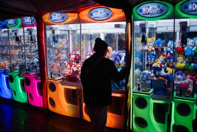 A visitor plays a plush toy crane claw game at the Christmas market and fairground in the Jardin des Tuileries gardens in central Paris, on November 24, 2025. (Photo by Dimitar DILKOFF / AFP)