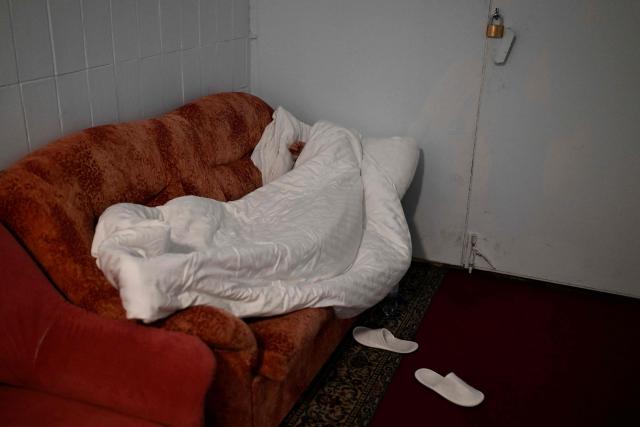 A person lies on the sofa in the hotel's underground shelter during an air attack in Kyiv early on November 25, 2025, amid the Russian invasion of Ukraine. Powerful explosions rocked Ukraine's capital Kyiv, an AFP journalist heard, as the air force issued a countrywide missile warning early November 25, 2025. (Photo by Sergei GAPON / AFP)