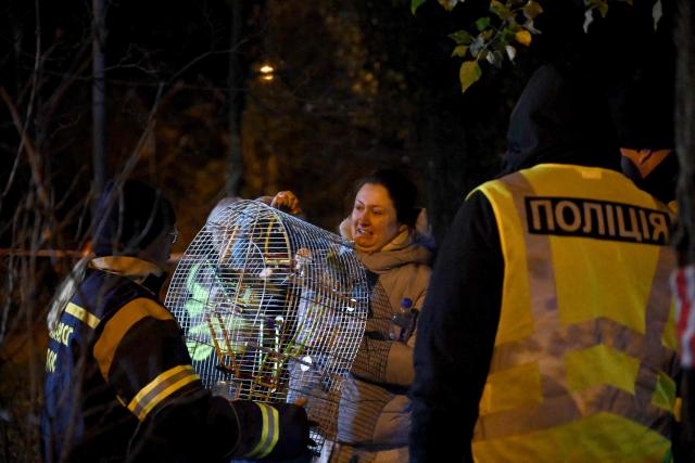 A rescuer hands over a cage with a saved parrot to its owner outside her damaged residential building following Russian missiles and drones strikes in Kyiv on November 25, 2025, amid Russian invasion in Ukraine. Powerful explosions rocked Ukraine's capital Kyiv, an AFP journalist heard, as the air force issued a countrywide missile warning early November 25, 2025. (Photo by Genya SAVILOV / AFP)