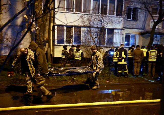 Firefighters carry a body outside a damaged residential building following Russian missiles and drones strikes in Kyiv on November 25, 2025, amid Russian invasion in Ukraine. Powerful explosions rocked Ukraine's capital Kyiv, an AFP journalist heard, as the air force issued a countrywide missile warning early November 25, 2025. (Photo by Genya SAVILOV / AFP)