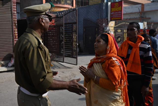 A Hindu devotee interacts with a policeman standing guard near Ram Temple in Ayodhya on November 25, 2025, ahead of Indian Prime Minister Narendra Modi’s visit. (Photo by Sajjad  HUSSAIN / AFP)