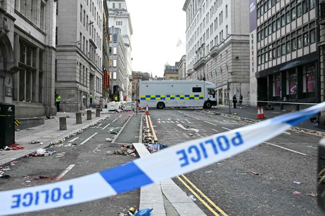 (FILES) Police officers stand at a cordon on in Water Street in Liverpool, north-west England on May 27, 2025, after a car ploughed in to crowds gathered to watch an open-top bus victory parade for Liverpool's Premier League trophy parade. A British man is due to go on trial on November 25, 2025 accused of driving his car into crowds at Liverpool Football Club's Premier League victory parade in May and injuring dozens of people. Paul Doyle, 54, has pleaded not guilty to 31 alleged offences, including charges of causing grievous bodily harm (GBH) with intent, wounding with intent, affray and dangerous driving. (Photo by Paul ELLIS / AFP)