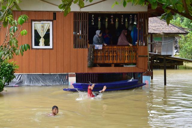 Children play in floodwaters in the Ban Yakang area of Mueang district in Thailand's southern province of Narathiwat on November 25, 2025, as severe flooding affected thousands of people in the country's south following days of heavy rain. (Photo by Madaree TOHLALA / AFP)
