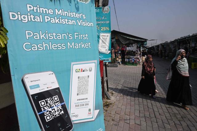 Women walk past an advertisement promoting digital cashless payment using QR (quick response) codes at a market in Islamabad on November 25, 2025. (Photo by Farooq NAEEM / AFP)