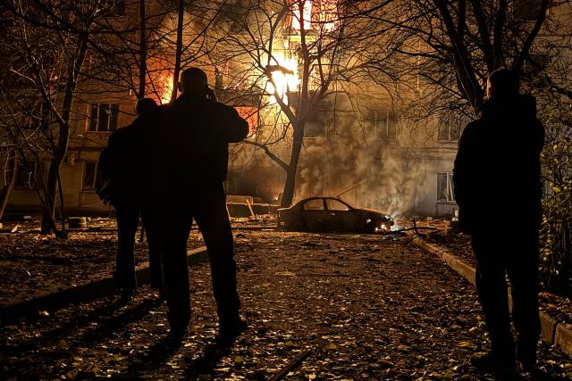 Local residents look on as a residential building burns following an air attack in Zaporizhzhia on November 25, 2025, amid the Russian invasion of Ukraine. (Photo by Darya NAZAROVA / AFP)