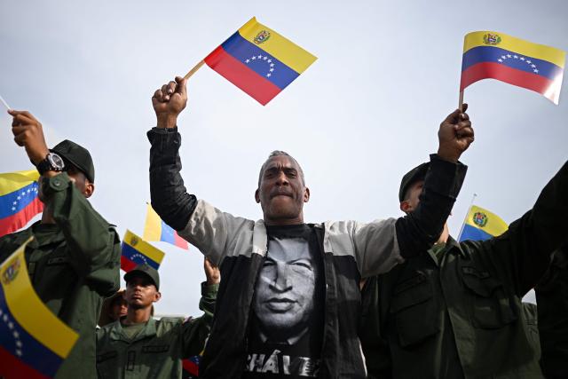 A supporter of Venezuela’s President Nicolas Maduro wears a T-shirt with an image of former Venezuelan President Hugo Chavez during a military ceremony at Fuerte Tiuna in Caracas on November 25, 2025. (Photo by Federico PARRA / AFP)