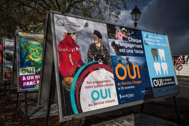 Voting posters in favor of an initiative for compulsory civic duty for all is seen in a street in Geneva, on November 25, 2025. The Swiss will vote on November 30, 2025 on replacing men's current military service requirement with a compulsory civic duty for all, with backers and opponents alike claiming to be championing women's rights. As part of Switzerland's direct democratic system, voters will also be weighing in on whether to slap new taxes on the super-rich to help finance the country's effort against climate change. (Photo by Fabrice COFFRINI / AFP)