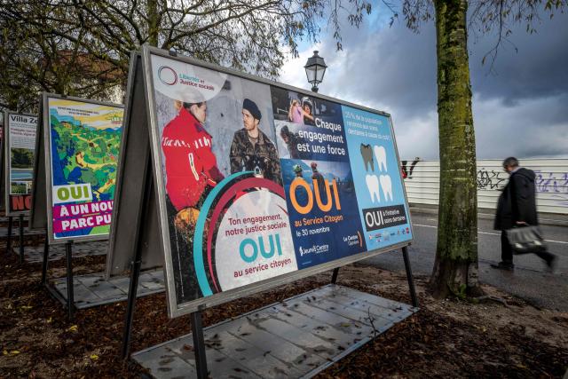 A man walks past voting posters in favor of an initiative for compulsory civic duty for all is seen in a street in Geneva, on November 25, 2025. The Swiss will vote on November 30, 2025 on replacing men's current military service requirement with a compulsory civic duty for all, with backers and opponents alike claiming to be championing women's rights. As part of Switzerland's direct democratic system, voters will also be weighing in on whether to slap new taxes on the super-rich to help finance the country's effort against climate change. (Photo by Fabrice COFFRINI / AFP)