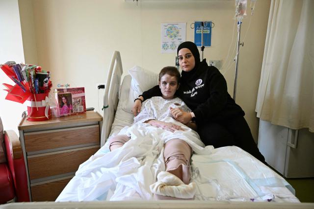EDITORS NOTE: Graphic content / Amani Bazzi (R) poses for a picture beside her eldest daughter Aseel at a hospital in Beirut on November 25, 2025, after being gravely wounded in an Israeli military strike on September 21, 2025, in the southern Lebanese town of Bint Jbeil. In one afternoon, Amani Bazzi went from being a doting mother-of-four to a widow grieving three young children. An Israeli strike in south Lebanon killed them as the family was returning home after having lunch with her parents. (Photo by Joseph EID / AFP)