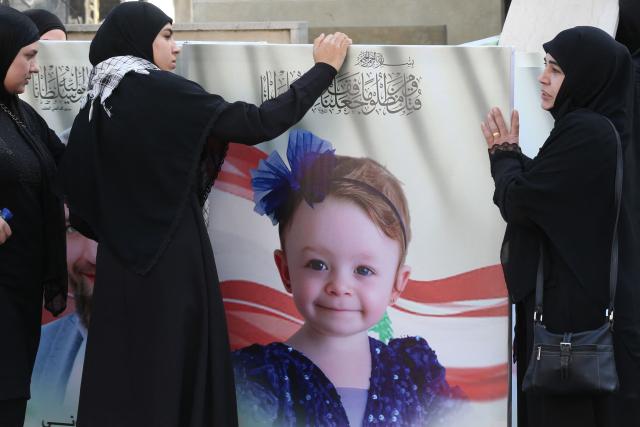 (FILES) Women stand beside a portrait of Cylan, a Lebanese toddler killed in an Israeli strike along with her twin brother, sister and father two days earlier, during their funeral in Bint Jbeil, in southern Lebanon, on September 23, 2025. In one afternoon, Amani Bazzi went from being a doting mother-of-four to a widow grieving three young children. An Israeli strike in south Lebanon killed them as the family was returning home after having lunch with her parents. (Photo by MAHMOUD ZAYYAT / AFP)