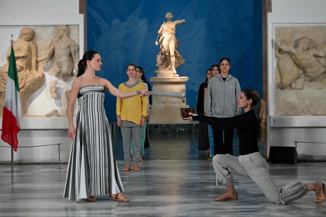 Greek actress Mary Mina (L) on the role of High Priestess takes part in the flame lighting ceremony during a rehearsal of the lighting of the Olympic flame, for the Olympic Winter Games Milano Cortina 2026, at the Museum of ancient Olympia, in Olympia, on November 25, 2025. (Photo by Aris MESSINIS / AFP)
