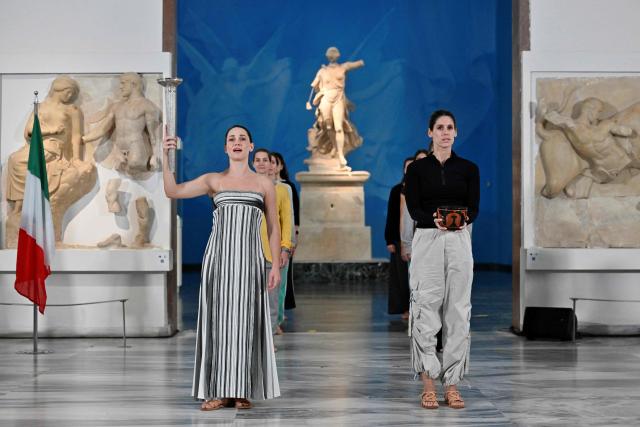 Greek actress Mary Mina (L) on the role of High Priestess takes part in the flame lighting ceremony during a rehearsal of the lighting of the Olympic flame, for the Olympic Winter Games Milano Cortina 2026, at the Museum of ancient Olympia, in Olympia, on November 25, 2025. (Photo by Aris MESSINIS / AFP)