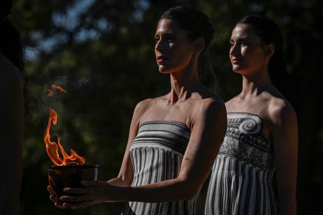 Greek actress Mary Mina on the role of High Priestess carries a a pot with the Olympic Flame as part of an emergency rehearsal of the lighting of the Olympic flame for the Milano-Cortina 2026 Winter Olympic Games ceremony, in the ancient stadium of Olympia at the archaeological site, birthplace of the ancient Olympics in southern Greece, on November 24, 2025. (Photo by Aris MESSINIS / AFP)