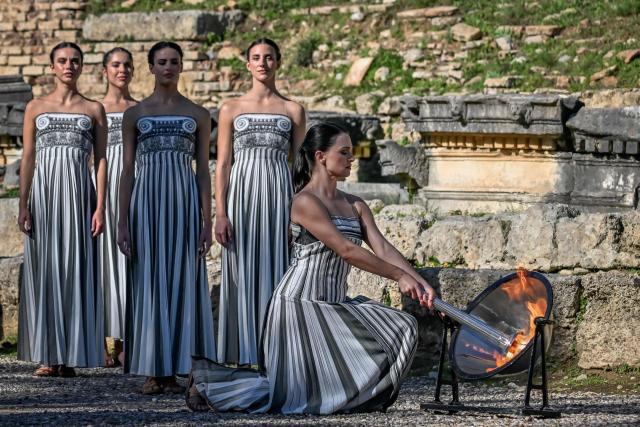Greek actress Mary Mina on the role of High Priestess lights the Olympic Flame from a solar mirror as part of an emergency rehearsal of the lighting of the Olympic flame for the Milano-Cortina 2026 Winter Olympic Games ceremony, in the ancient stadium of Olympia at the archaeological site, birthplace of the ancient Olympics in southern Greece, on November 24, 2025. (Photo by Aris MESSINIS / AFP)