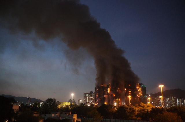 Thick smoke and flames rise as a major fire engulfs several apartment blocks at the Wang Fuk Court residential estate in Hong Kong's Tai Po district on November 26, 2025. Four people died after multiple blocks in a Hong Kong residential estate went up in flames on November 26, with local media earlier reporting that some residents were trapped. (Photo by Yan ZHAO / AFP)