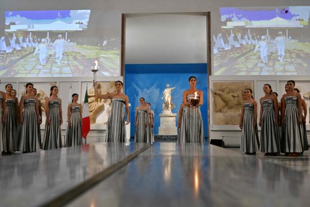 Greek actress Mary Mina (L), playing the role of the High Priestess, takes part in the flame lighting ceremony of the Olympic flame, for the Olympic Winter Games Milano Cortina 2026, at the Museum of ancient Olympia, in Olympia on November 26, 2025. (Photo by Aris MESSINIS / AFP)