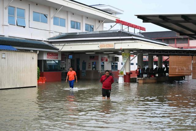 People wade through the water next to a flooded hospital in Kangar in northern Malaysia's Perlis state on November 26, 2025, as severe flooding affected thousands of people in the region following days of heavy rain. Flooding in Malaysia from days of heavy rain has swept through eight states, with forecasters predicting more rain in the coming days. More than 27,000 people were evacuated to dozens of temporary shelters this week, with one death recorded in one of the worst-hit states, Kelantan, on the northeastern coast, according to rescue officials. (Photo by MOHD RASFAN / AFP)