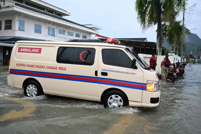 An ambulance drives through the water next to a flooded hospital in Kangar in northern Malaysia's Perlis state on November 26, 2025, as severe flooding affected thousands of people in the region following days of heavy rain. Flooding in Malaysia from days of heavy rain has swept through eight states, with forecasters predicting more rain in the coming days. More than 27,000 people were evacuated to dozens of temporary shelters this week, with one death recorded in one of the worst-hit states, Kelantan, on the northeastern coast, according to rescue officials. (Photo by MOHD RASFAN / AFP)