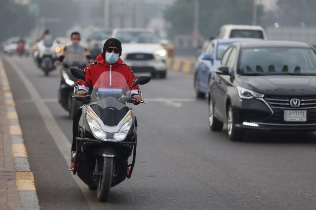 An Iraqi man wearing a facemask rides a scooter on Al-Sinak Bridge in central Baghdad as thick smog envelops the city on November 26, 2025. (Photo by AHMAD AL-RUBAYE / AFP)