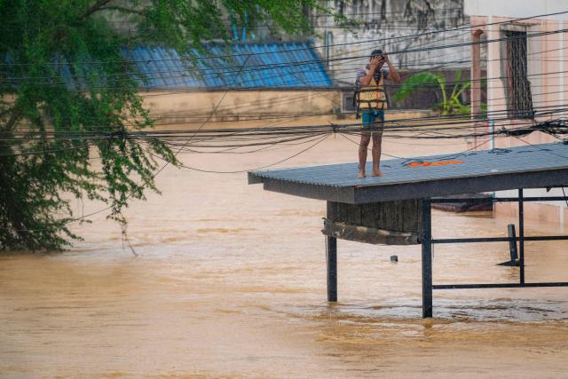 A man reacts as he stands on a roof next to high flood waters in Hat Yai in Thailand's southern Songkhla province on November 26, 2025, as severe flooding affected thousands of people in the country's south following days of heavy rain. Tens of thousands of people in Thailand and neighbouring Malaysia were displaced by widespread flooding, with streets submerged, homes inundated and at least 34 dead, officials said November 26. (Photo by Arnun Chonmahatrakool / THAI NEWS PIX / AFP)