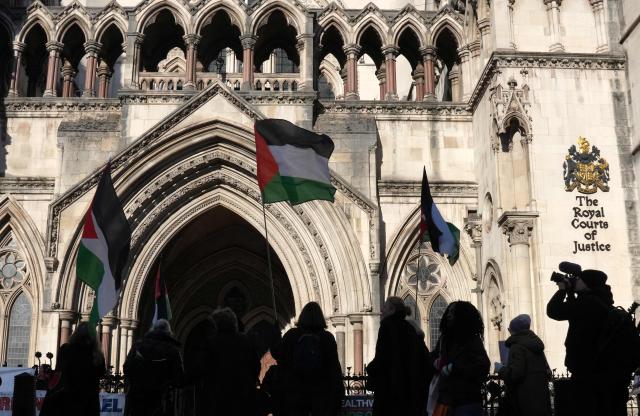 Protesters hold placards and flags during a demonstration in support of "Defend Our Juries" and their campaign against the ban on Palestine Action, outside the Royal Courts of Justice, Britain's High Court, in central London on November 26, 2025. The co-founder of activist group Palestine Action will Wednesday challenge a UK government ban under anti-terror laws that has led to mass arrests, sparking free speech and civil liberties concerns. (Photo by CARLOS JASSO / AFP)