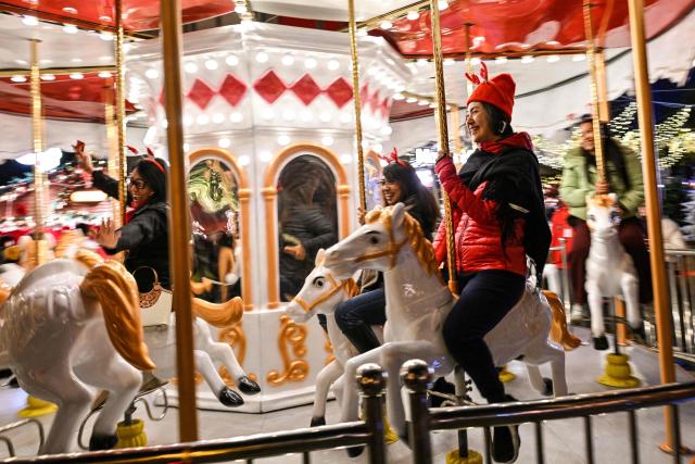 People in festive attire ride a carousel on the first day of the Christmas market at Huangpu district in Shanghai on November 26, 2025. (Photo by Hector RETAMAL / AFP)