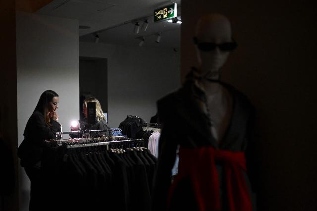 TOPSHOT - Customers use flashlights of their mobile phones while visiting a Mango clothing shop during Black Friday sales, as power is cut off, in Kyiv, on November 26, 2025, amid the Russian invasion of Ukraine.  (Photo by Sergei GAPON / AFP)