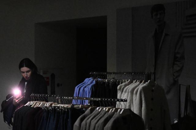 A customer uses the flashlight of their mobile phone while visiting a Mango clothing shop during Black Friday sales, as power is cut off, in Kyiv, on November 26, 2025, amid the Russian invasion of Ukraine.  (Photo by Sergei GAPON / AFP)