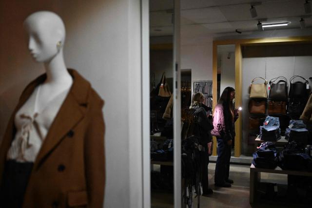 Customers use flashlights of their mobile phones while visiting a Mango clothing shop during Black Friday sales, as power is cut off, in Kyiv, on November 26, 2025, amid the Russian invasion of Ukraine.  (Photo by Sergei GAPON / AFP)