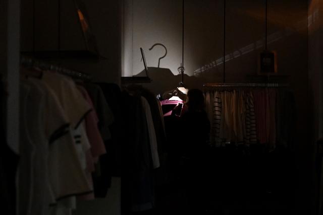 A customer uses the flashlight of their mobile phone while visiting a Mango clothing shop during Black Friday sales, as power is cut off, in Kyiv, on November 26, 2025, amid the Russian invasion of Ukraine.  (Photo by Sergei GAPON / AFP)