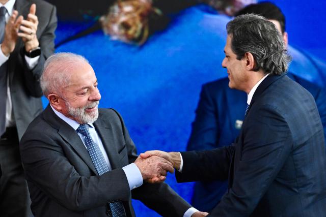 Brazil's President Luiz Inacio Lula da Silva (L) and his Finance Minister Fernando Haddad shake hands during the signing ceremony of the new Income Tax Law at the Planalto Palace in Brasilia, on November 26, 2025. (Photo by Evaristo Sa / AFP)