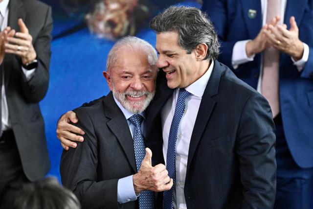 Brazil's President Luiz Inacio Lula da Silva (L) and his Finance Minister Fernando Haddad embrace during the signing ceremony of the new Income Tax Law at the Planalto Palace in Brasilia, on November 26, 2025. (Photo by Evaristo Sa / AFP)