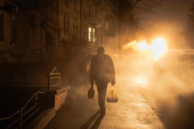 A man walks under the light coming from an excavator on a non-illuminated street during blackout hours in Kyiv on November 26, 2025, following Russian missile and drone attacks on Ukrainian energy infrastructure amid the Russian invasion of Ukraine. (Photo by Roman PILIPEY / AFP)