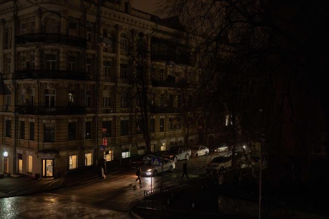 People walk on a non-illuminated street as the light comes from a cafe using electricity from a power generator during blackout hours in Kyiv on November 26, 2025, following Russian missile and drone attacks on Ukrainian energy infrastructure amid the Russian invasion of Ukraine. (Photo by Roman PILIPEY / AFP)
