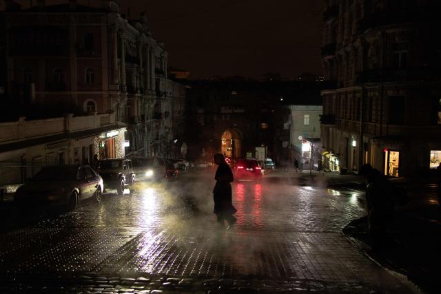 A woman crosses the road on a non-illuminated street during blackout hours in Kyiv on November 26, 2025, following Russian missile and drone attacks on Ukrainian energy infrastructure amid the Russian invasion of Ukraine. (Photo by Roman PILIPEY / AFP)