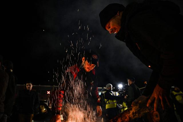 Protesters stand beside a fire during a demonstration of French agricultural unions FNSEA and Jeunes Agriculteurs of the Seine-Maritime and Eure departments to protest the EU-Mercosur agreements and taxes affected their sector, on the Tancarville Bridge, in Tancarville, on November 26, 2025. (Photo by Lou BENOIST / AFP)