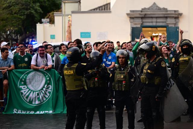 Riot police officers stand guard as fans of Palmeiras wait for the arrival of their team at a hotel in Lima on November 26, 2025, ahead of the Copa Libertadores final football match between Brazil's Palmeiras and Brazil's Flamengo in the Peruvian capital on November 29. (Photo by ERNESTO BENAVIDES / AFP)