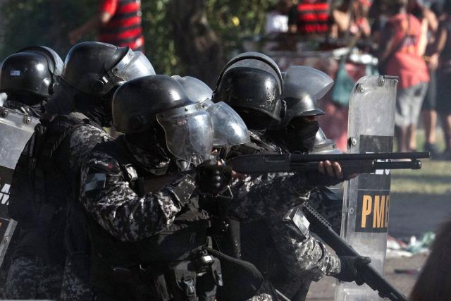Military Police officers fire rubber bullets during clashes as fans of Brazil's Flamengo accompany a bus carrying the team on its way to Galeao International Airport in Rio de Janeiro, Brazil, on November 26, 2025. Flamengo team flew to Lima Wednesday to face Palmeiras in the Libertadores Cup final match, which will take place on November 29. (Photo by Pablo PORCIUNCULA / AFP)