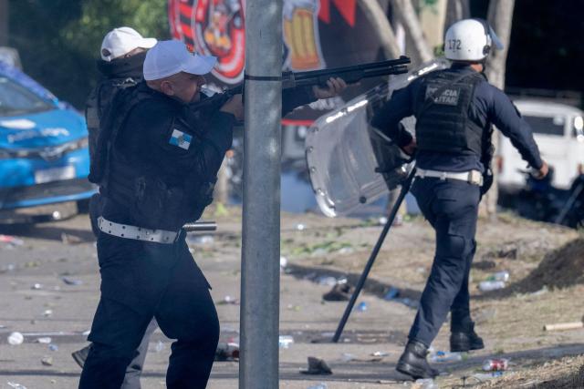 Military Police officers fire rubber bullets during clashes as fans of Brazil's Flamengo accompany a bus carrying the team on its way to Galeao International Airport in Rio de Janeiro, Brazil, on November 26, 2025. Flamengo team flew to Lima Wednesday to face Palmeiras in the Libertadores Cup final match, which will take place on November 29. (Photo by Pablo PORCIUNCULA / AFP)