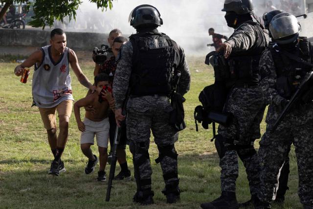 Fans of Brazil's Flamengo who were accompanying a bus carrying the team on its way to the Galeao international airport, try to protect themselves from tear gas due to disturbs, in Rio de Janeiro, Brazil, on November 26, 2025. Flamengo team flew to Lima Wednesday to face Palmeiras in the Libertadores Cup final match, which will take place on November 29. (Photo by Pablo PORCIUNCULA / AFP)