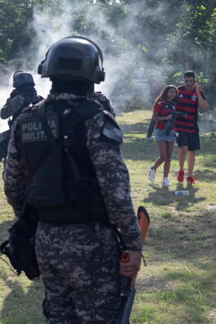 Fans of Brazil's Flamengo who were accompanying a bus carrying the team on its way to the Galeao international airport, try to protect themselves from tear gas due to disturbs, in Rio de Janeiro, Brazil, on November 26, 2025. Flamengo team flew to Lima Wednesday to face Palmeiras in the Libertadores Cup final match, which will take place on November 29. (Photo by Pablo PORCIUNCULA / AFP)