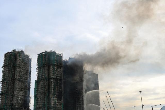 TOPSHOT - Firefighters spray water on flames as a major fire burns through several apartment blocks at the Wang Fuk Court residential estate in Hong Kong's Tai Po district on November 27, 2025. The death toll from a high-rise fire in Hong Kong has risen to at least 44, officials said on November 27 as the blaze still smoldered and police said three suspects were arrested. (Photo by Peter PARKS / AFP)