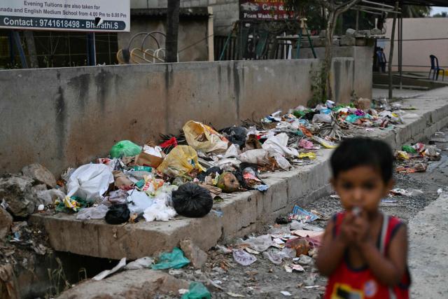 In this photograph taken on November 7, 2025, a child stands near a footpath strewn with garbage at the under construction Panathur Railway Station Road in Bengaluru. Home to nearly 12 million people and state capital of Karnataka, Bengaluru is the "Silicon Valley" of the world's fifth biggest economy -- hosting thousands of start-ups, outsourcing firms, and global tech giants from Google to Microsoft. Yet its flagship Outer Ring Road (ORR) business district is clogged with traffic, pocked with potholes, and often flooded during the monsoon. (Photo by Idrees MOHAMMED / AFP) / TO GO WITH 'India-Politics-Technology-Environment' FOCUS