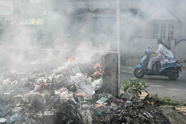 In this photograph taken on November 12, 2025, a woman rides past a burning garbage dump formed by littering near a residential area in Bengaluru. Home to nearly 12 million people and state capital of Karnataka, Bengaluru is the "Silicon Valley" of the world's fifth biggest economy -- hosting thousands of start-ups, outsourcing firms, and global tech giants from Google to Microsoft. Yet its flagship Outer Ring Road (ORR) business district is clogged with traffic, pocked with potholes, and often flooded during the monsoon. (Photo by Idrees MOHAMMED / AFP) / TO GO WITH 'India-Politics-Technology-Environment' FOCUS