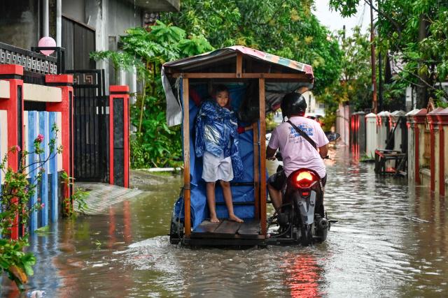 A man transports a child through the floodwaters on an inundated street following heavy rain at a residential area of Darul Imarah on the outskirts of Banda Aceh on November 27, 2025. (Photo by CHAIDEER MAHYUDDIN / AFP)