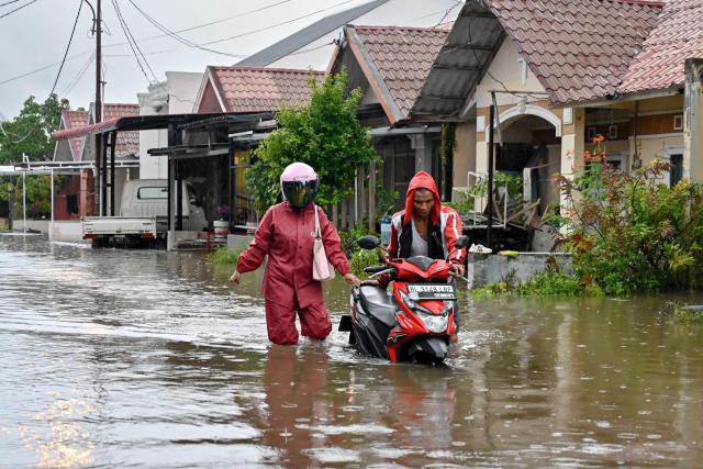 A man pushes his motorcycle through the floodwaters on an inundated street following heavy rain at a residential area of Darul Imarah on the outskirts of Banda Aceh on November 27, 2025. (Photo by CHAIDEER MAHYUDDIN / AFP)
