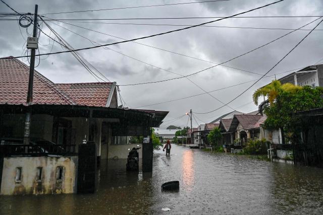 A man wades through the floodwaters on an inundated street following heavy rain at a residential area of Darul Imarah on the outskirts of Banda Aceh on November 27, 2025. (Photo by CHAIDEER MAHYUDDIN / AFP)