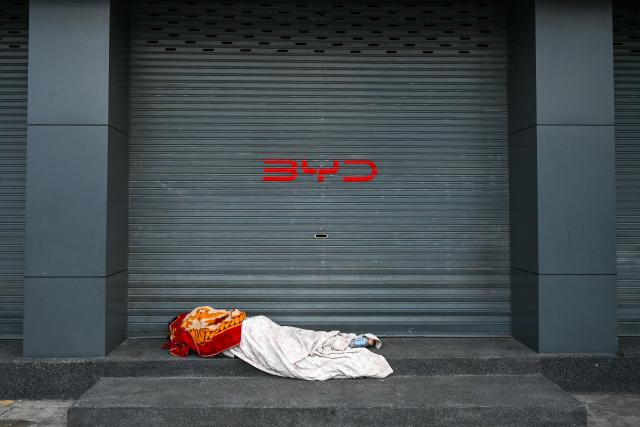 A man sleeps on the stairs in front of a car showroom in Phnom Penh on November 27, 2025. (Photo by TANG CHHIN Sothy / AFP)