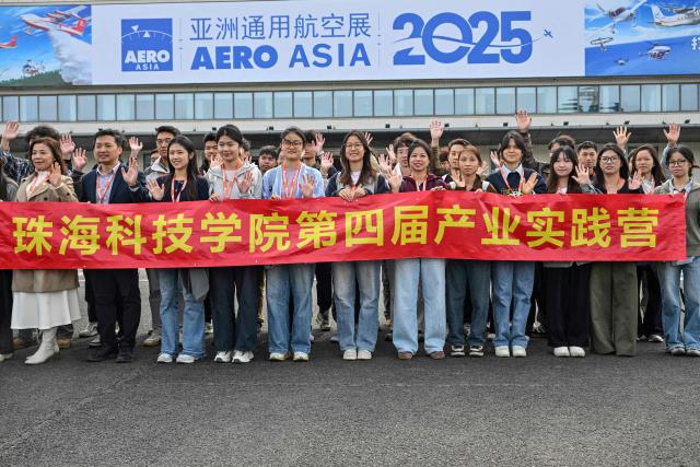 Members of a student group pose for a picture during the Aero Asia 2025 in Zhuhai, in southern China's Guangdong province on November 27, 2025. Aero Asia 2025 is an international aviation and aerospace exhibition that runs between November 27 and 30. (Photo by Hector RETAMAL / AFP)